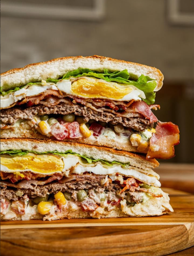 Xis bacon da Voni aberto ao meio, com carne, bacon, ovo, queijo e salada